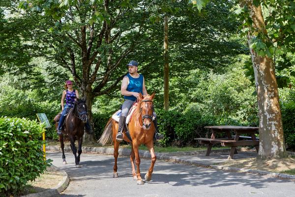 Un hombre y una mujer montados a caballo por la vía verde